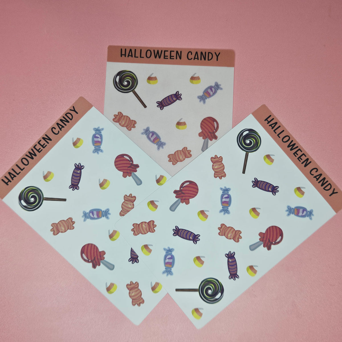Sticker sheets with a variety of Halloween candy on a pink background with candy and pens around the sticker sheet
